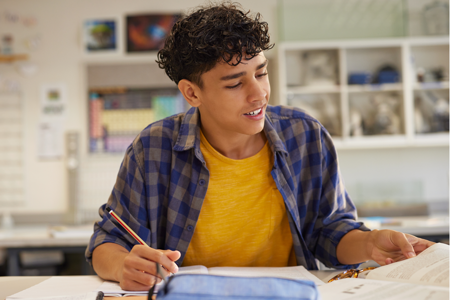 Young boy sitting at a desk in a classroom, writing in a notebook.